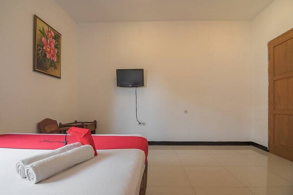 A hotel room with a bed, a TV mounted on the wall, a wooden door, and a painting on the wall. - RedDoorz @ Maribaya Street 2 (Lembang)