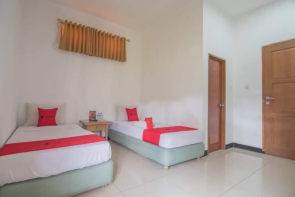 A hotel room with two beds, a nightstand, a wooden door, and a window with curtains.