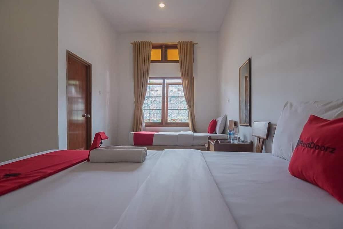 A hotel room with a bed, a desk, a chair, a window with curtains, and a door.