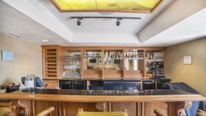 A bar area with a wooden bar counter, shelves with bottles, glasses, and a ceiling skylight.