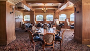 A spacious dining area with a high ceiling, wooden beams, and large windows offering a view of the outdoors.