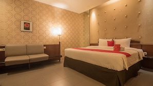 A hotel room with a bed, a sofa, a bedside table, a lamp, and a wall with a geometric pattern. - RedDoorz Plus @ Cipaganti Street 3 (Bandung)