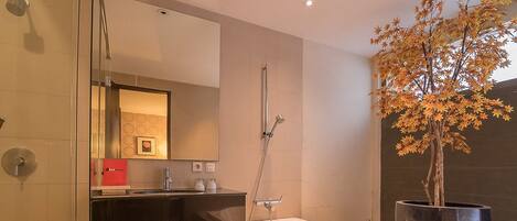 A modern bathroom with a glass shower enclosure, a white bathtub, and a large potted tree.