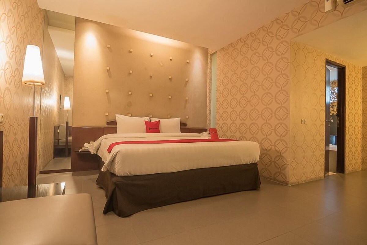 A hotel room with a bed, bedside tables, a mirror, and a patterned wall.