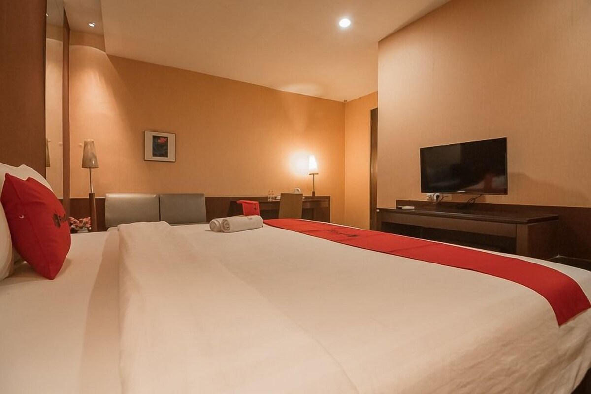 A hotel room with a large bed, a flat-screen TV, a desk, and a lamp.