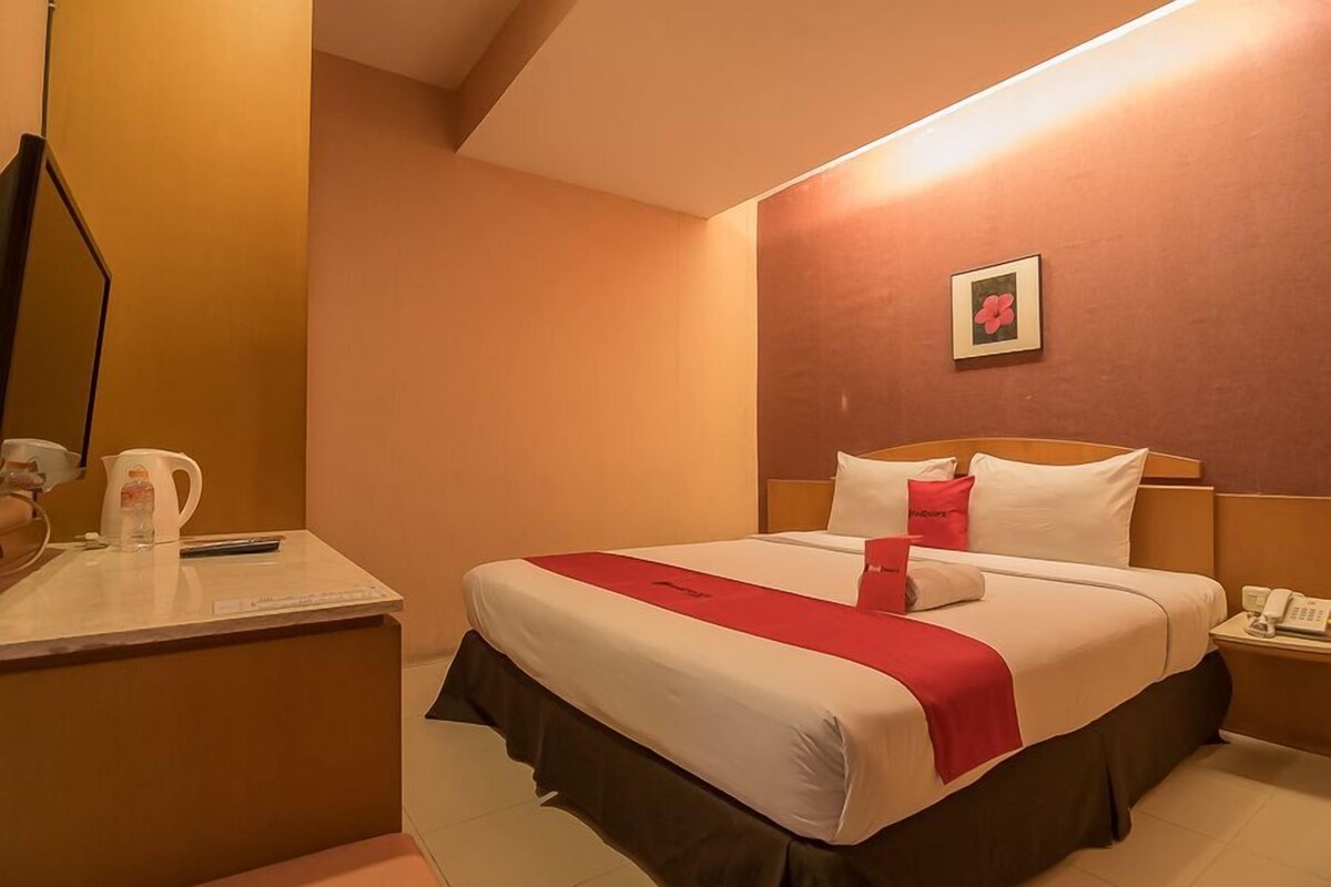 A hotel room with a bed, bedside table, and a mirror.