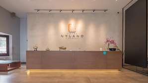 A reception desk with a logo for 'NYLAND GIPAGANTI HOTEL' and a sign indicating a wheelchair-accessible area. - RedDoorz Plus @ Cipaganti Street 3 (Bandung)