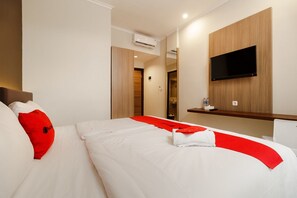 A hotel room with a bed, a TV mounted on the wall, and a small shelf with a bottle.