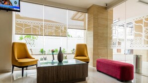 Een moderne lobby met twee gele fauteuils, een salontafel met glazen blad en een rode bank.