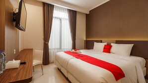 Een hotelkamer met een groot bed, een houten bureau, een flatscreen televisie en een raam met gordijnen.