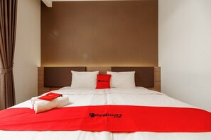 A hotel room with a neatly made bed, a red throw blanket, and a pillow with a logo.