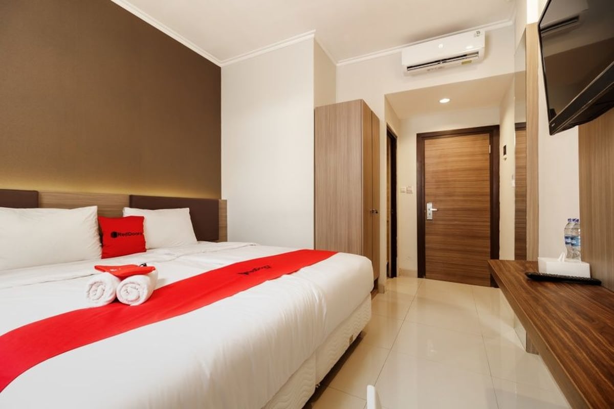 Une chambre d’hôtel avec un grand lit, une télévision, une porte en bois et un banc.