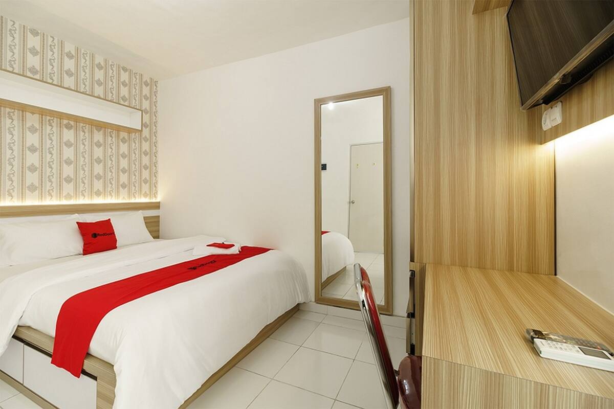 Een hotelkamer met een bed, bureau, spiegel en televisie.