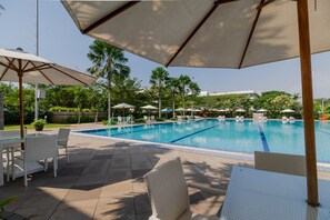 A pool area with lounge chairs and umbrellas, surrounded by palm trees and greenery.