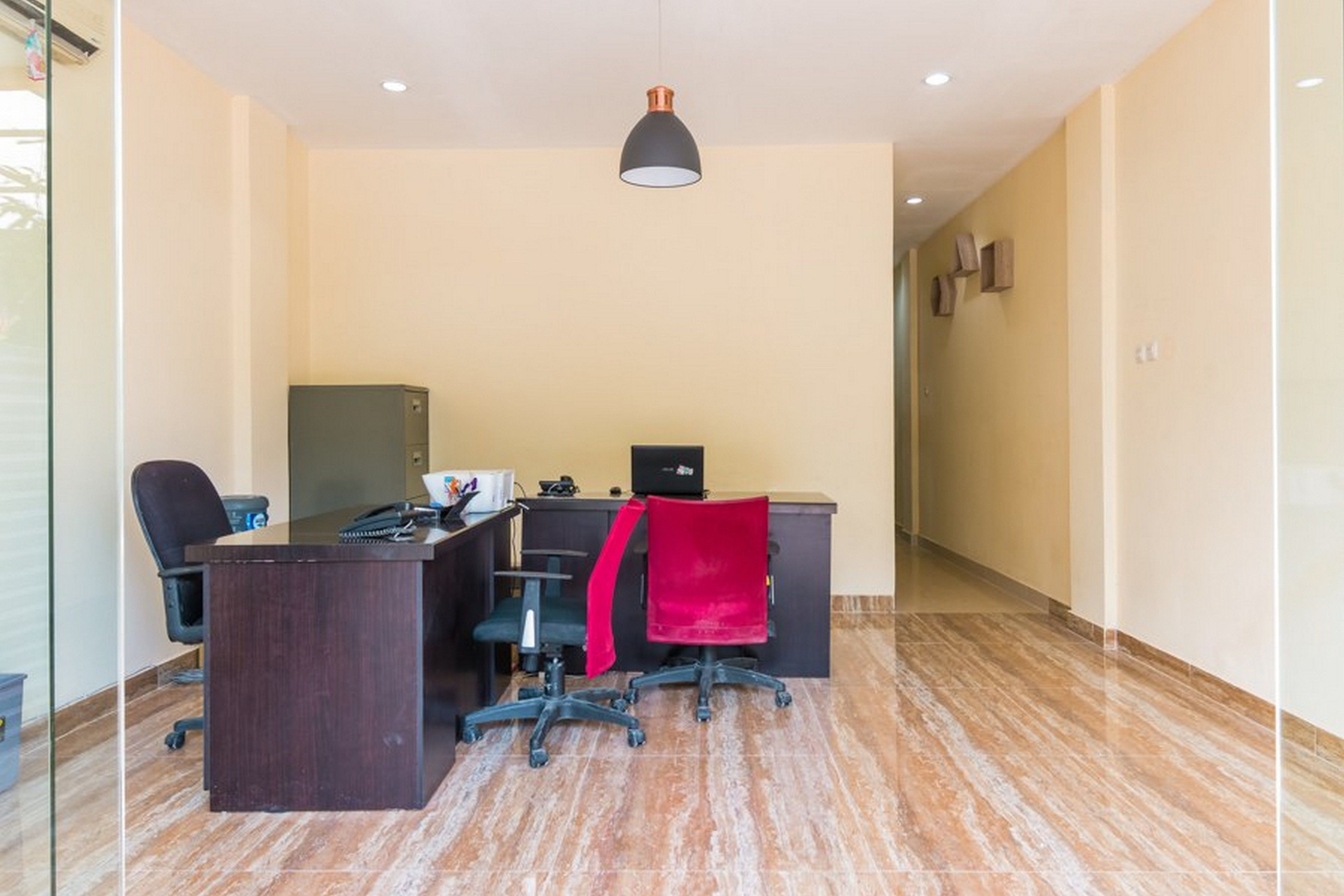 A modern office space with a dark wooden desk, two black office chairs, a red chair, a computer, and a black lamp.