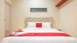 A neatly made bed with a red and white bedspread, a pillow with a red logo, and a sign on the wall that reads "Believe in the good in the world." - RedDoorz @ Tebet Barat 2 (Jakarta)
