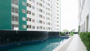 A swimming pool adjacent to a multi-story building with balconies. - RedDoorz Apartment near Bundaran Satelit Surabaya (Surabaya)