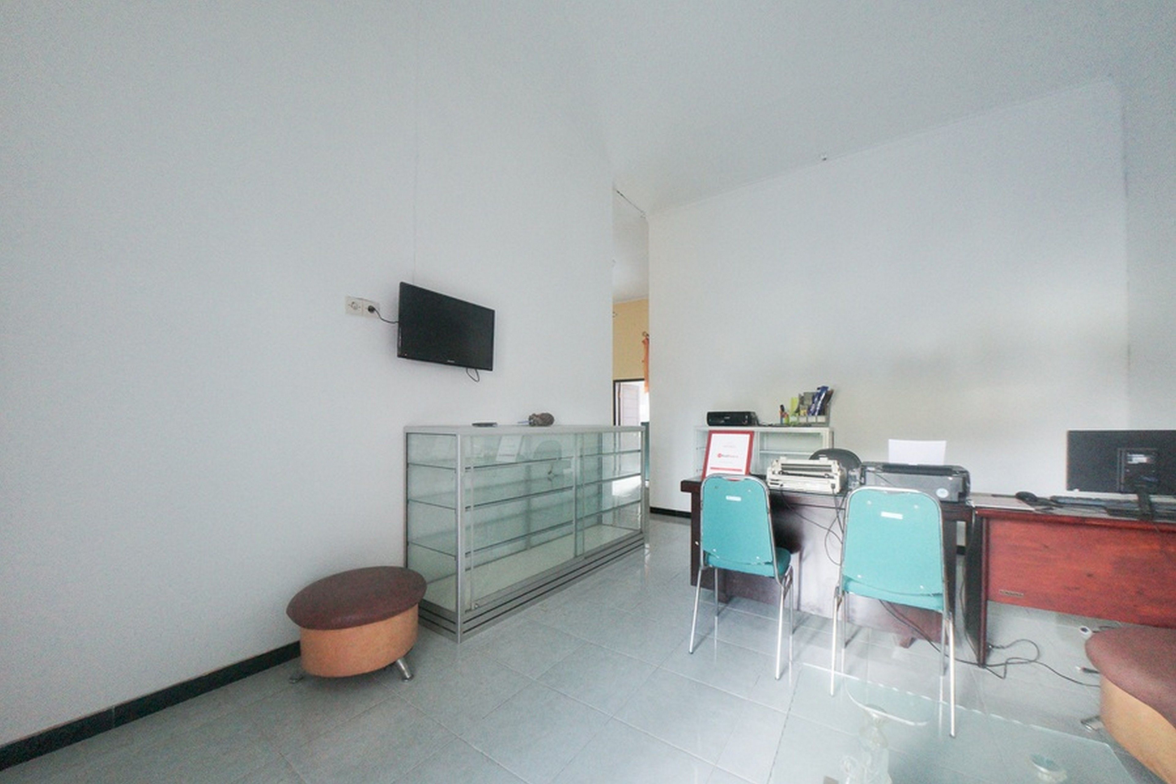 A room with a glass cabinet, two chairs, a desk with a computer, and a television mounted on the wall.