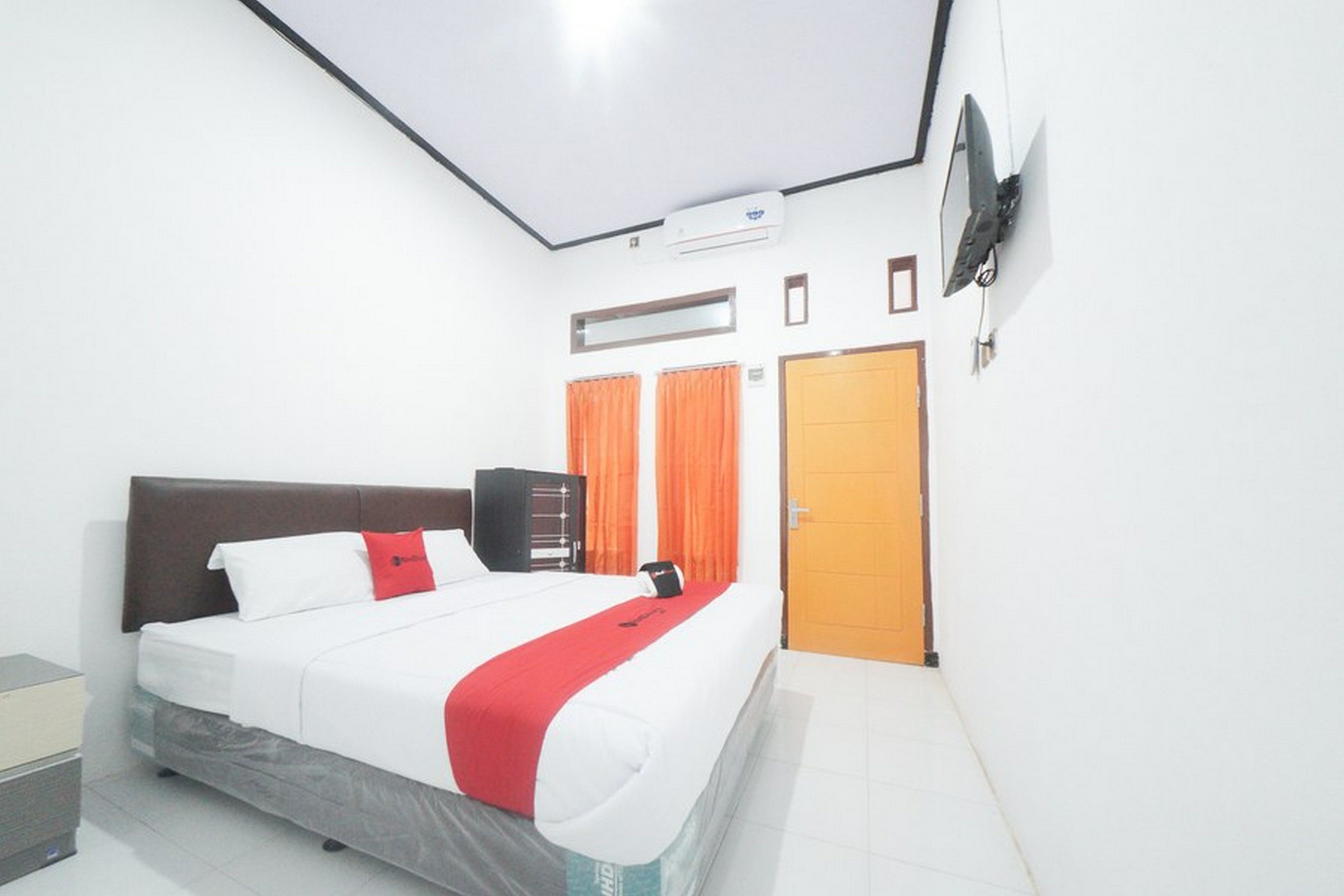 A hotel room with a bed, a TV mounted on the wall, an air conditioning unit, and a door.