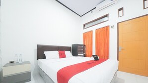 A hotel room with a bed, a nightstand, an air conditioning unit, a door, and orange curtains. - RedDoorz Syariah near Mall Roxy Banyuwangi 2 (Banyuwangi)