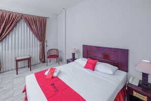 Una habitación de hotel con una cama grande, una mesita de noche de madera con una lámpara, una silla y una pequeña mesa.