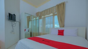 A hotel room with a bed, a TV mounted on the wall, and a window with curtains.