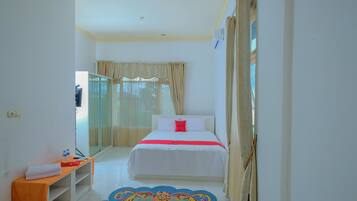 A hotel room with a bed, a bedside table with a towel, a small table with bottles, and a patterned rug.