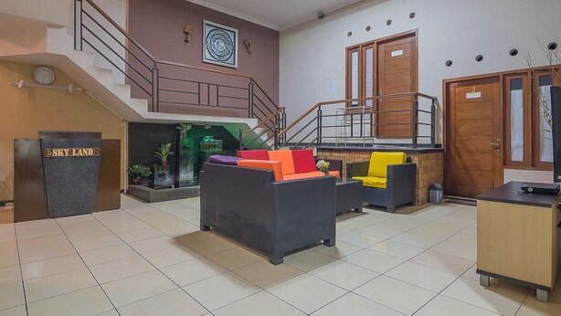 Un vestíbulo de hotel con una recepción, una escalera, un sofá con cojines coloridos y una pequeña mesa.