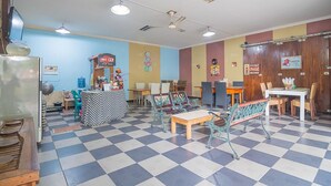 Una cafetería con suelo a cuadros, mesas de madera y sillas de metal verde.