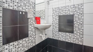 Un baño con un lavamanos blanco, un dispensador de jabón rojo y un espejo.