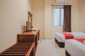 A hotel room with two beds, a desk with a chair, a wooden bench, a window with curtains, and an air conditioning unit.