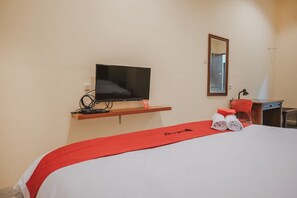A hotel room with a bed, a TV on a shelf, a desk with a chair, and a mirror on the wall.