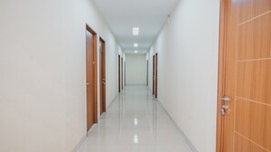 A long, narrow hallway with wooden doors on both sides and a tiled floor. - RedDoorz Plus near Plaza Blok M (Jakarta)