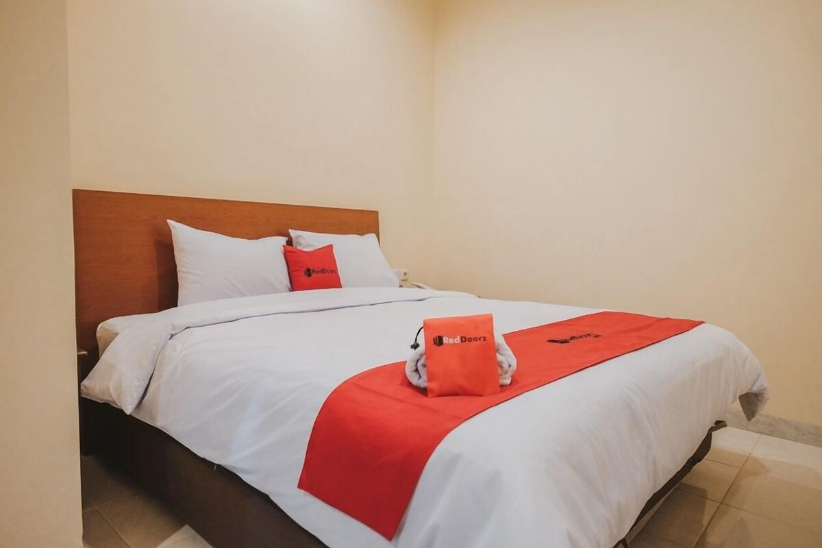 Ein Hotelzimmer mit Bett, weißer Bettwäsche, einem Holz-Kopfteil und einer roten Decke.