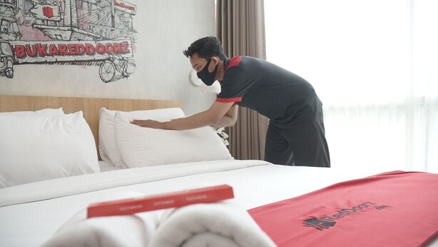 A hotel room with a neatly made bed, a red blanket with the hotel's logo, and a wall mural. - RedDoorz Plus near Plaza Blok M (Jakarta)