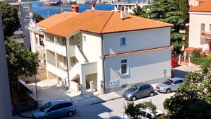 A two-story building with a red-tiled roof, a visible balcony on the second floor, and a parking area with several cars. - Holiday apartment "Dunja", only 500m from the beach (Pula)