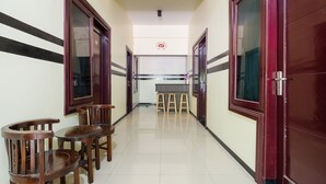 Un couloir avec des chaises et des tables en bois, un coin cuisine avec des tabourets, et une porte avec un panneau de verre.
