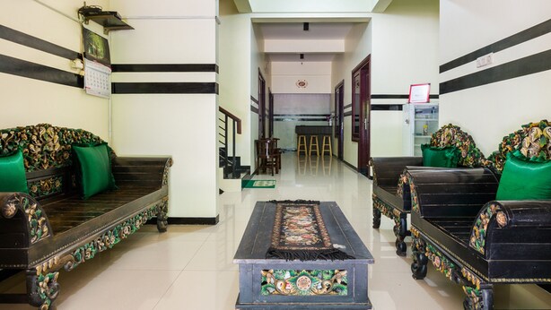 Un hall d’entrée avec des canapés richement décorés et une table centrale, un escalier en arrière-plan et une porte avec une pancarte.