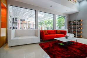Un salon moderne avec un canapé blanc, un canapé rouge et un tapis rouge. On y trouve une bibliothèque avec des plantes et une table basse blanche.