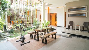 A spacious indoor area with a wooden bench, a table, and an exercise bike. There are potted plants and a staircase in the background. - Reddoorz Syariah Near Transmart MX Malang (Malang)