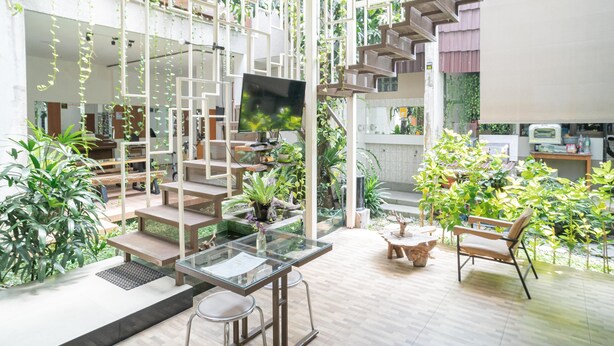 A spacious living area with a modern staircase, a flat-screen TV, and various plants. - Reddoorz Syariah Near Transmart MX Malang (Malang)