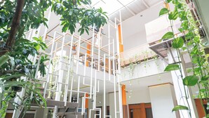A multi-level atrium with a modern white and orange color scheme, featuring a central white column structure, hanging plants, and a staircase. - Reddoorz Syariah Near Transmart MX Malang (Malang)