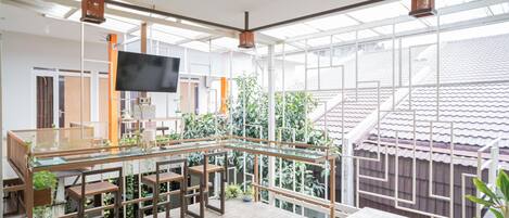 A spacious living area with a glass dining table, wooden chairs, and a flat-screen TV mounted on the wall.