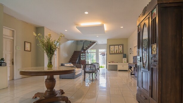 A spacious living area with a large wooden cabinet, a dining table, and a staircase leading to another level. - RedDoorz near UPI Setiabudi 2 (Bandung)