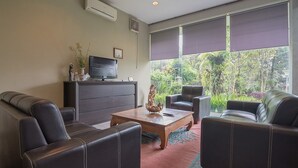 A modern living room with leather sofas, a wooden coffee table, a flat-screen TV, and a large window with blinds. - RedDoorz near UPI Setiabudi 2 (Bandung)