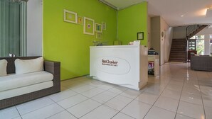 A reception area with a green wall, a white reception desk, and a brown sofa. - RedDoorz near UPI Setiabudi 2 (Bandung)