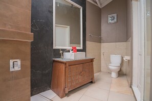 A bathroom with a wooden vanity, a white sink, a large mirror, a toilet, and a shower area. - RedDoorz near UPI Setiabudi 2 (Bandung)