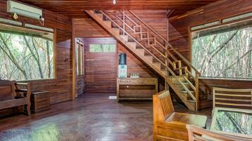 A wooden interior with a staircase, wooden furniture, and large windows offering a view of trees.