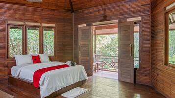A wooden cabin bedroom with a bed, a red throw, and a view of the outdoors through a door.