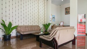 A lobby with a beige sofa, a black armchair, and a coffee table. There are potted plants and a framed certificate on the wall. - RedDoorz Syariah near Universitas Jenderal Soedirman (Purwokerto)